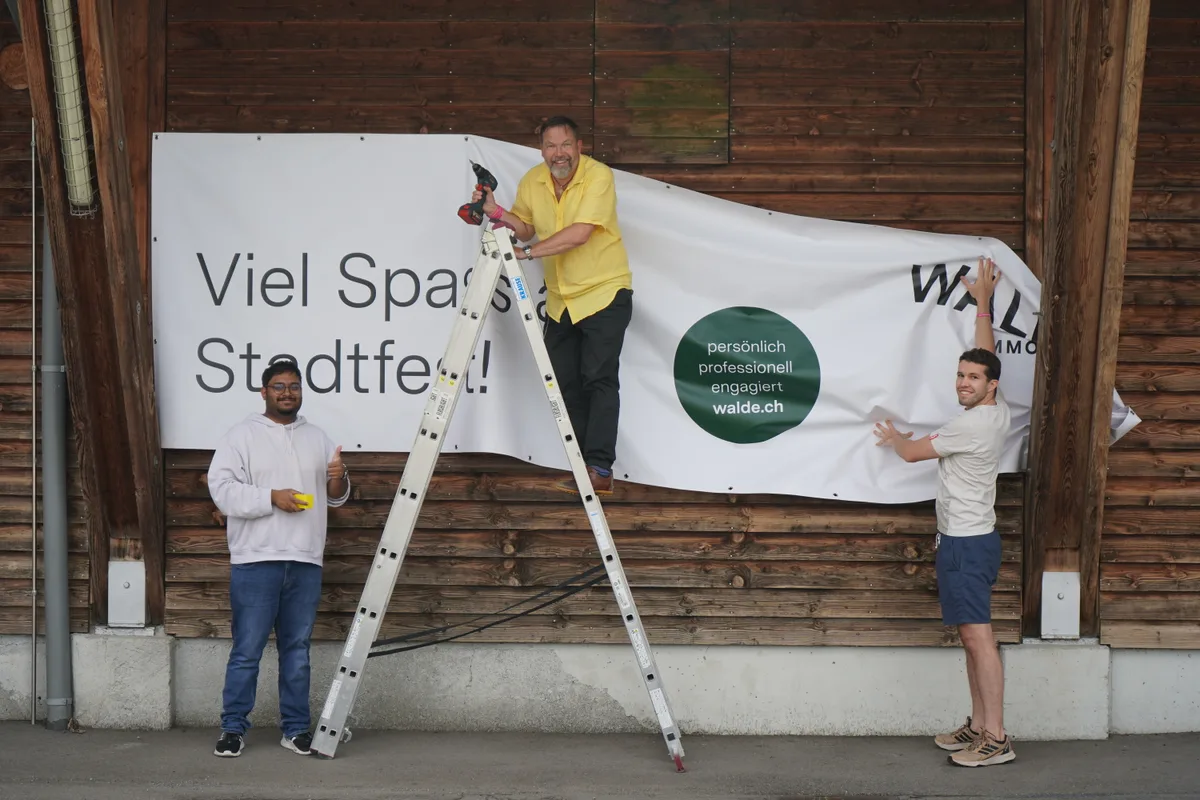 Drei Menschen halten ein Banner fest.